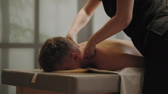 man is relaxing and enjoying massage in spa salon, professional masseuse is stroking neck of adult male patient