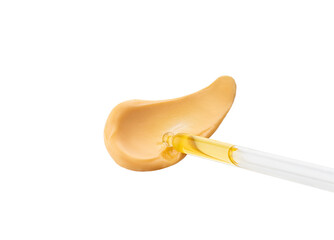 Cosmetic pipette with drops of oil or serum, on the background of orange cosmetic cream smear. Close-up, selective focus