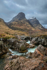 Gorgeous landscape image of vibrant River Coe flowing beneath snowcapped mountains in Scottish Highlands