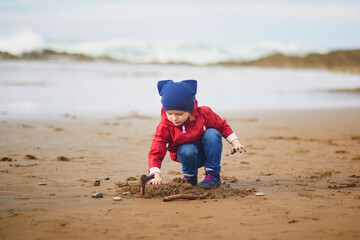Adorable toddler girl playing on the sand beach at Atlantic coast of Zumaia, Basque Country, Spain