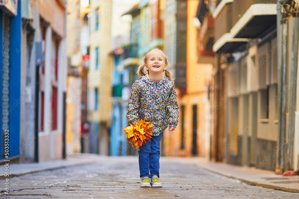 Wall mural happy girl with bunch of autumn leaves on a street of fishing village of bermeo, basque country, spa