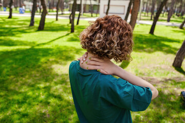 Redhead woman wearing green tee from back having neck or shoulder pain. Injury or muscle spasm. Female massaging her neck. Health care and medical concept.