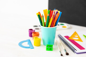 Time to return back to school. Bright colourful green yellow, blue stationery, paints, pencils, markers, brushes. black board on background. White alarm clock. Copy space for text. Autumn, September