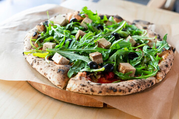 vegan pizza with arugula or rucola tofu olives and tomatoes close-up wooden board vegetarian food healthy eating