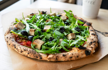 vegan pizza with arugula or rucola tofu olives and tomatoes close-up wooden board vegetarian food healthy eating