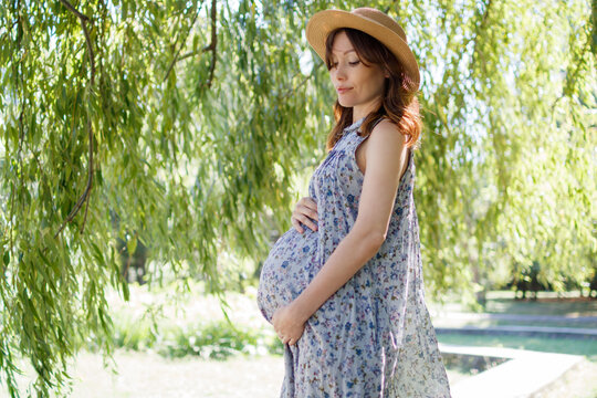 Pregnant woman outdoors in the park on a summer day. Place for text.