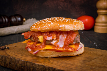 Burger with meat cheese and bacon with red onion and tomato sauce on board