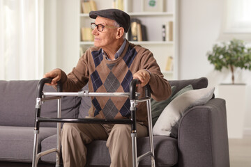 Elderly man sitting on a sofa and holding onto a walker - obrazy, fototapety, plakaty