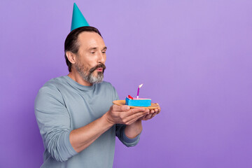 Profile side photo of mature man blow candle dreamy delicious dessert isolated over violet color...