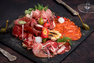 slicing of different meat on black stone plate with spices and fried garlic macro close up