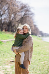 pensive woman looking away while holding little daughter outdoors.