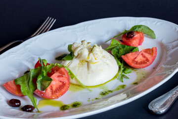 Salad with buratta cheese and tomatoes on white plate on dark table