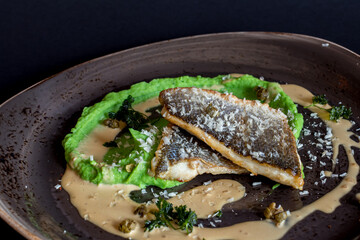 Fried sea bass fillet with sauce on dark plate macro close up