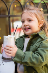 happy girl holding glass with milkshake on blurred foreground.