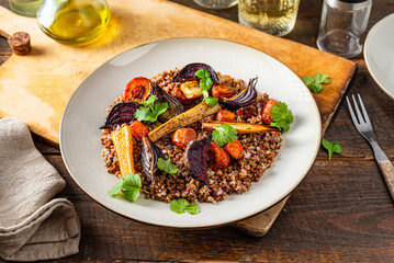 Buckwheat salad with roasted root vegetables. Rustic wooden table.