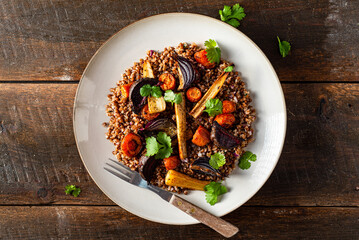 Buckwheat salad with roasted root vegetables. Rustic wooden table.