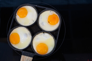 Top view of make fried eggs on black frying pan on electric stove for breakfast.