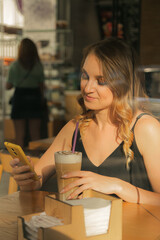 Business woman sitting in a cafe with coffee, texting on a smartphone, view through the window