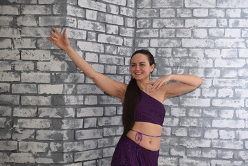 A beautiful dancer in oriental attire poses in a dance style in the studio against a brick wall