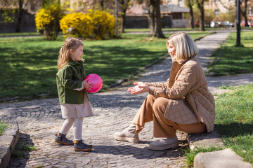 side view of joyful girl holding ball while having fun with mom in park.