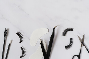 Beauty concept image including tools, products and equipment for eyelash extensions. Black and white colour theme set against a white background with copy space.