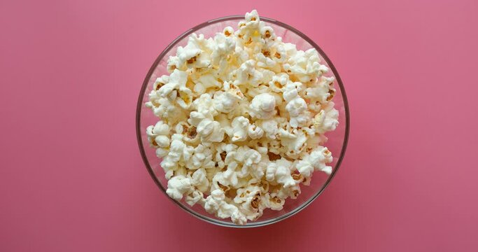 A glass transparent bowl is filled with popcorn on a pink background. 4K stop motion animation