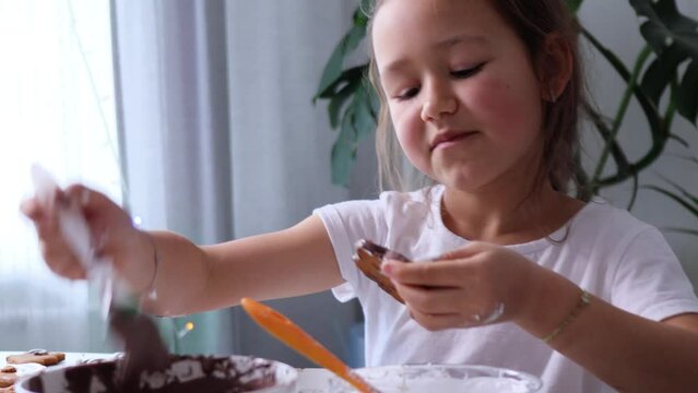 Funny happy girl is dancing while decorates homemade gingerbread with chocolate icing, than eating the cookie, 4K footage