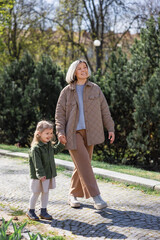 Obraz premium full length of happy and stylish woman with daughter walking in spring park.