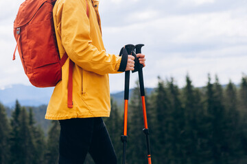 Close up Hiker with trekking poles goes against mountain landscape. Hiking and travel concept
