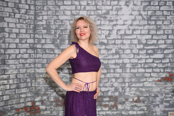 A beautiful blonde dancer in an oriental outfit in the studio against a brick wall