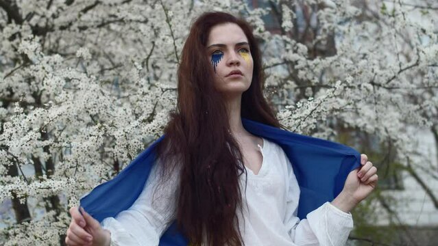 Young attractive girl portrait with Ukrainian flag in the spring cherry garden 