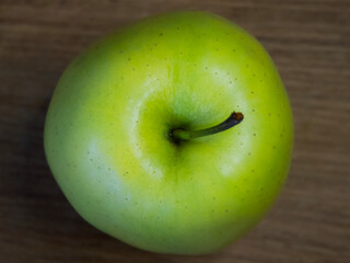 The Reinette Simirenko is an antique apple variety. The fruit has tender, crisp, greenish white flesh with a subacid flavor. A green apple on a wooden tabletop, close-up.