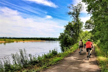 Beneath a blue sky with white clouds on a summer day in Wisconsin, three cyclists on a dirt path...