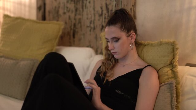 Chica joven con pantalón y blusa negra interactuando con tablet en habitación de hotel