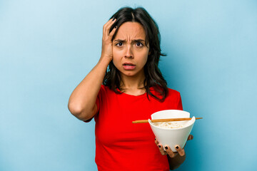 Young hispanic woman eating noodles isolated on blue background being shocked, she has remembered...