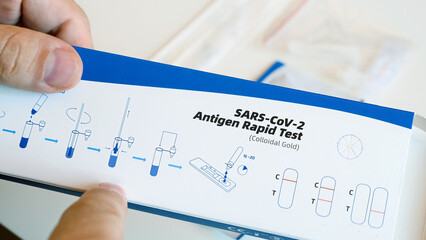 Man is holding a box with a rapid covid test and reading the instructions. Steps of self-testing for the covid virus at home are written In Thai language. Epidemic, control disease