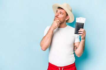 Young caucasian traveler man holding passport isolated on blue background looking sideways with doubtful and skeptical expression.