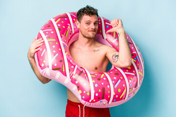 Young caucasian man holding an inflatable donut isolated on blue background feels proud and self...