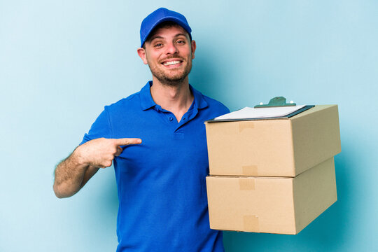 Young caucasian delivery man isolated on blue background person pointing by hand to a shirt copy space, proud and confident