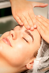 Obraz na płótnie Canvas Head massage. Beautiful caucasian young white woman receiving a head and forehead massage with closed eyes in a spa salon