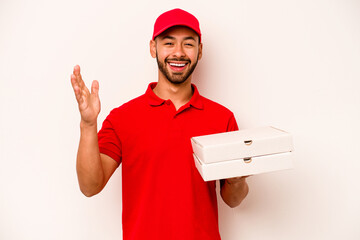 Young hispanic delivery man holding pizzas isolated on white background receiving a pleasant surprise, excited and raising hands.