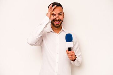 Young hispanic TV presenter isolated on blue background excited keeping ok gesture on eye.