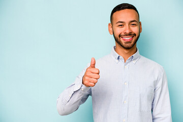 Young hispanic man isolated on blue background smiling and raising thumb up