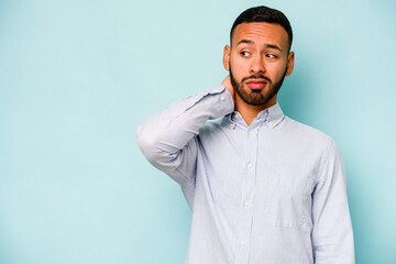 Young hispanic man isolated on blue background touching back of head, thinking and making a choice.