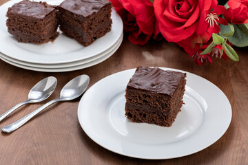 slice of chocolate cake covered with chocolate, served chilled, a bouquet of red roses next to the plate