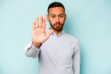 Young hispanic man isolated on blue background standing with outstretched hand showing stop sign,...