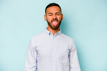 Young hispanic man isolated on blue background funny and friendly sticking out tongue.