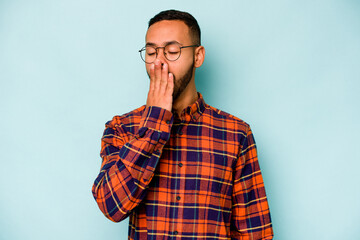 Young hispanic man isolated on blue background yawning showing a tired gesture covering mouth with hand.