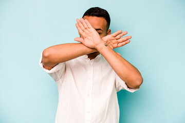 Young hispanic man isolated on blue background keeping two arms crossed, denial concept.