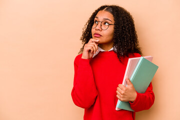 Young student African American woman isolated on beige background looking sideways with doubtful and skeptical expression.